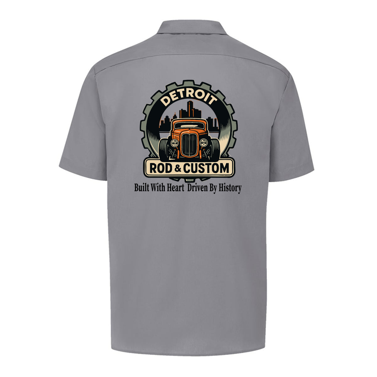 Back of a graphite grey Dickies short-sleeve work shirt with an orange hot rod coupe in a DETROIT ROD & CUSTOM gear badge over the Detroit skyline, with Built With Heart Driven By History below.