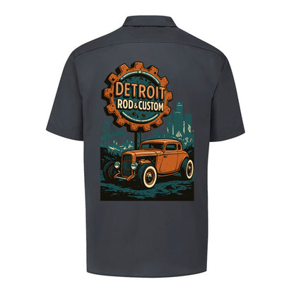 Back of a dark charcoal Dickies short-sleeve work shirt with an orange Atomic Coupe hot rod under a DETROIT ROD & CUSTOM gear badge.