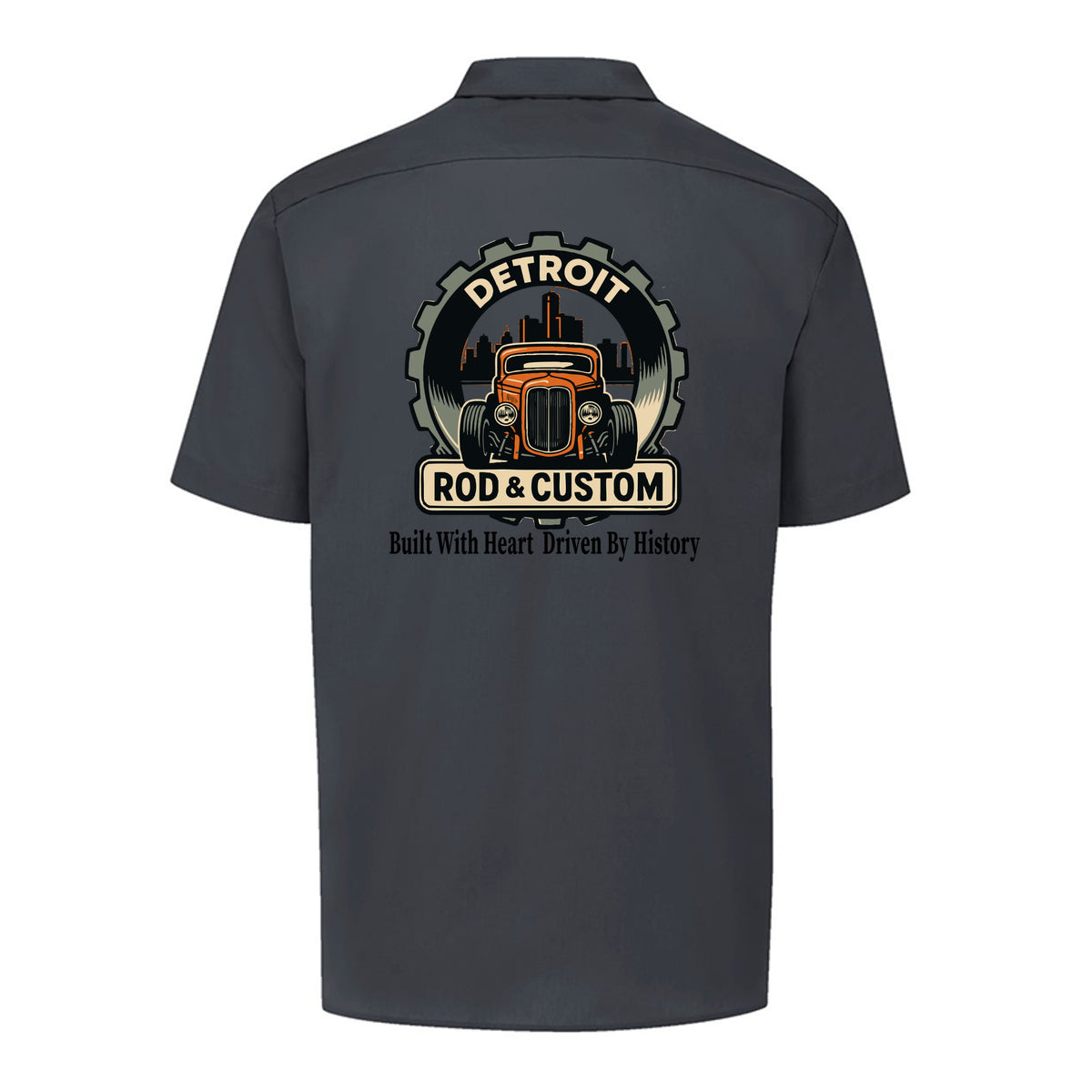 Back of a dark charcoal Dickies short-sleeve work shirt with an orange hot rod coupe in a DETROIT ROD & CUSTOM gear badge over the Detroit skyline, with Built With Heart Driven By History below.