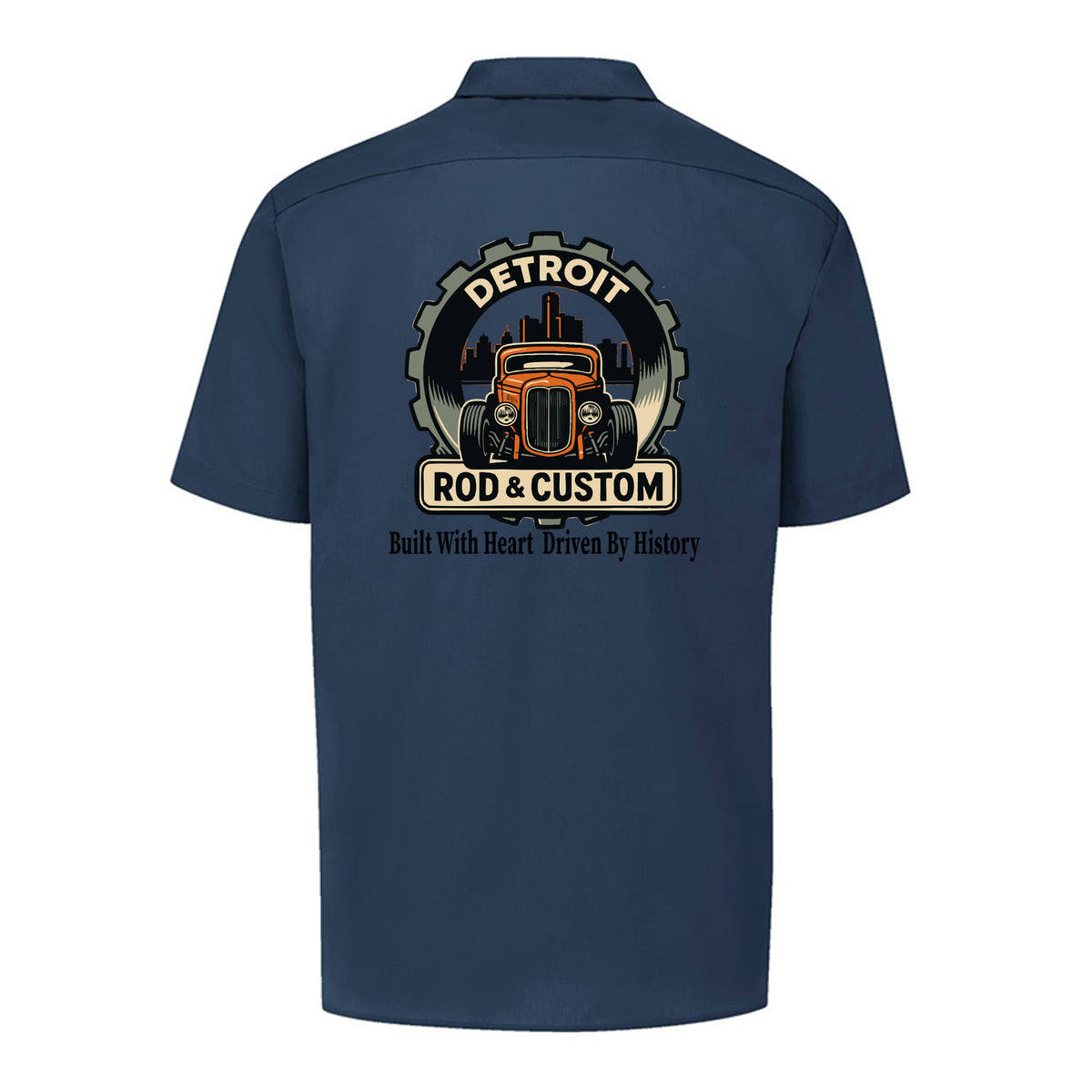 Back of a dark navy Dickies short-sleeve work shirt with an orange hot rod coupe in a DETROIT ROD & CUSTOM gear badge over the Detroit skyline, with Built With Heart Driven By History below.
