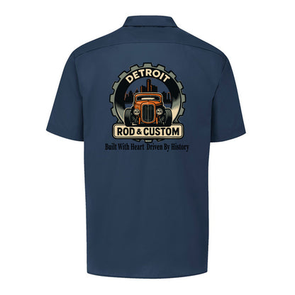 Back of a dark navy Dickies short-sleeve work shirt with an orange hot rod coupe in a DETROIT ROD & CUSTOM gear badge over the Detroit skyline, with Built With Heart Driven By History below.