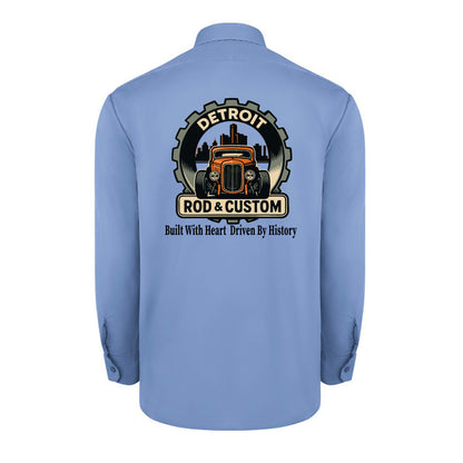 Back of a light blue Dickies long-sleeve work shirt with an orange hot rod coupe in a DETROIT ROD & CUSTOM gear badge over the Detroit skyline, with Built With Heart Driven By History below.