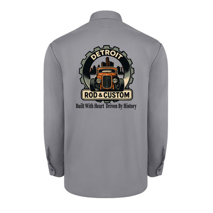 Back of a graphite grey Dickies long-sleeve work shirt with an orange hot rod coupe in a DETROIT ROD & CUSTOM gear badge over the Detroit skyline, with Built With Heart Driven By History below.