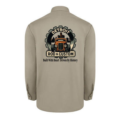 Back of a desert sand Dickies long-sleeve work shirt with an orange hot rod coupe in a DETROIT ROD & CUSTOM gear badge over the Detroit skyline, with Built With Heart Driven By History below.