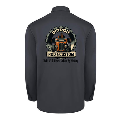 Back of a dark charcoal Dickies long-sleeve work shirt with an orange hot rod coupe in a DETROIT ROD & CUSTOM gear badge over the Detroit skyline, with Built With Heart Driven By History below.
