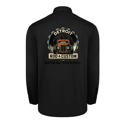 Back of a black Dickies long-sleeve work shirt with an orange hot rod coupe in a DETROIT ROD & CUSTOM gear badge over the Detroit skyline, with Built With Heart Driven By History below.